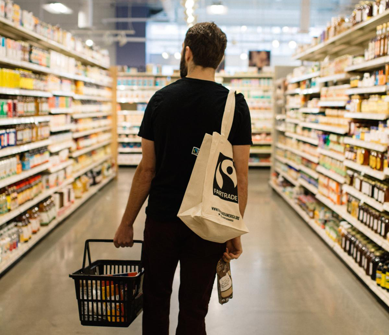 Homme vu de dos faisant ses courses dans un magasin FairTrade avec un sac un toile sur lequel est imprimé le logo "Fair Trade". © Fairtrade Belgium